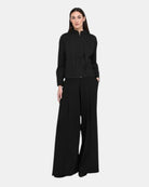 Model trägt LEEZZA OZAI N KÜ GALA schwarze Wide-Leg-Hose mit überlappender Vorderpartie und Seitentaschen